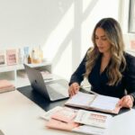 Woman in a studio office managing a beauty product business and preparing for content creation with a ring light and camera, illustrating non-service cosmetology jobs.