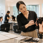 Experienced beauty instructor demonstrating hair sectioning on a mannequin head in a modern salon classroom with lesson notes, styling tools, and students practicing in the background.