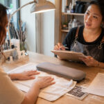 Nail technician reviews an intake form with a client whose natural hands rest at an organized manicure station before the service begins.